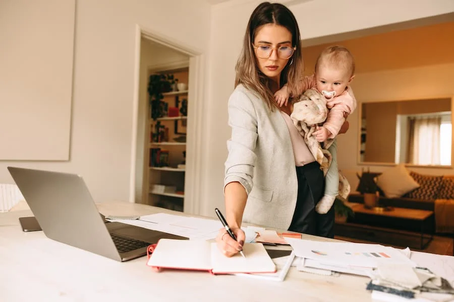 Mère épuisée par le burn-out parental, portant son enfant tout en télétravaillant