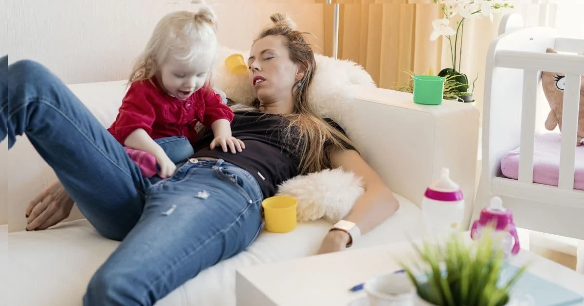 Femme épuisée allongée sur un canapé avec son enfant, illustrant le burn-out parental et la fatigue mentale des parents