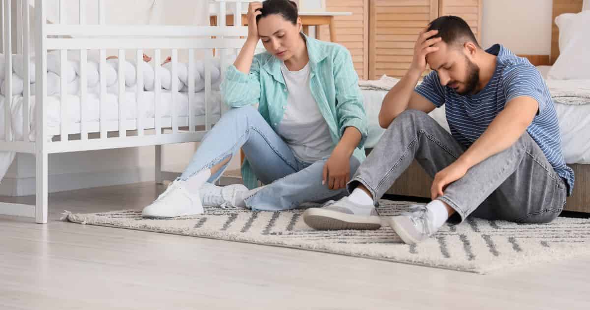 Deux parents au pied d’un lit, mains sur la tête, épuisés, illustrant les conséquences du burn-out parental sur la vie familiale