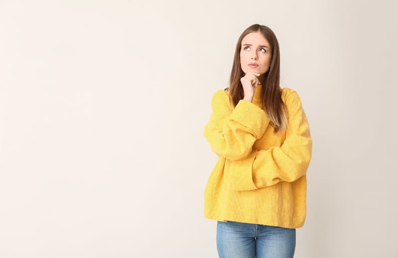 Femme en pull jaune assis et pensif, se demandant comment choisir un sophrologue à Genève.